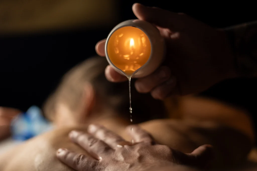 Terapeuta masażu aplikuje ciepły aromatyczny olejek ze świecy na dłoń klienta podczas zmysłowego zabiegu spa