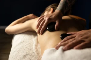 Terapeuta masażu wykonuje masaż gorącymi kamieniami bazaltowymi na plecach klienta, wspierając głębokie rozluźnienie i regenerację