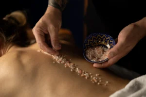 Terapeuta masażu aplikuje naturalny peeling solny na plecach klienta, przygotowując skórę do głębokich zabiegów