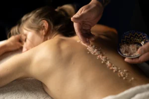 Terapeuta masażu wykonuje peeling ciała naturalnymi solami, połączony z relaksacyjnym masażem na plecach klienta